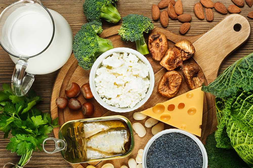 Distintos alimentos con calcio como la leche, el queso, sardinas, almendras y avellanas en una mesa