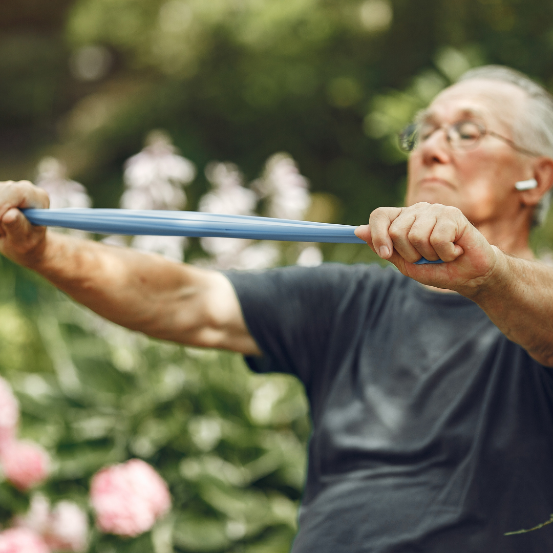 Un hombre mayor sostiene un palo con los brazos extendidos para realizar un ejercicio de espalda