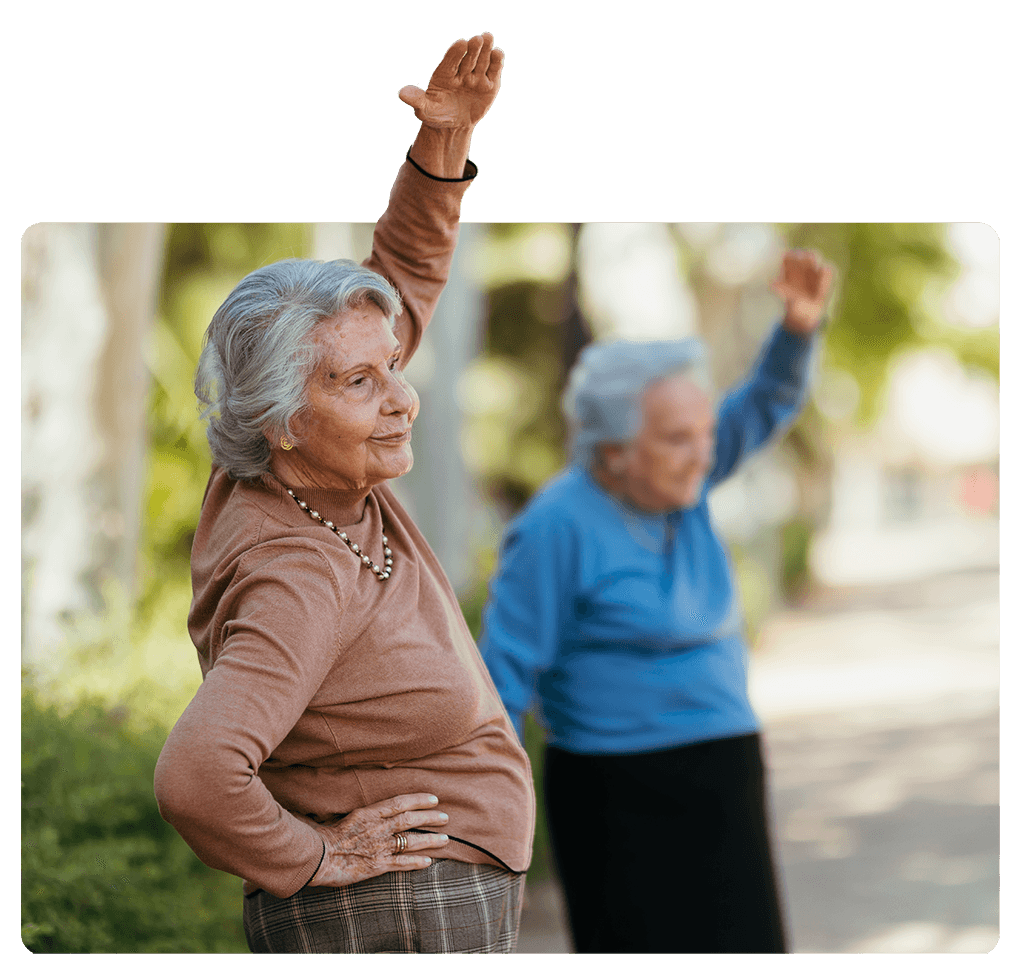 Una imagen silueteada de dos ancianas haciendo ejercicio con el brazo levantado en un parque.
