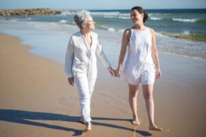Mujer mayor y mujer joven caminando descalzas por la playa, dirigiéndose hacia la cámara