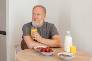 Abuelo desayunando zumo, leche y fruta