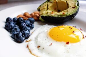 Plato con un huevo, un aguacate, almendras y arándanos