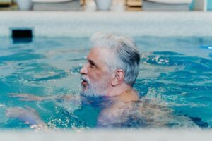 Hombre mayor con el pelo blanco y barba nadando en una piscina