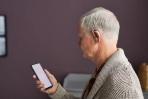 Hombre mayor de perfil con un audífono sujetando un móvildo 