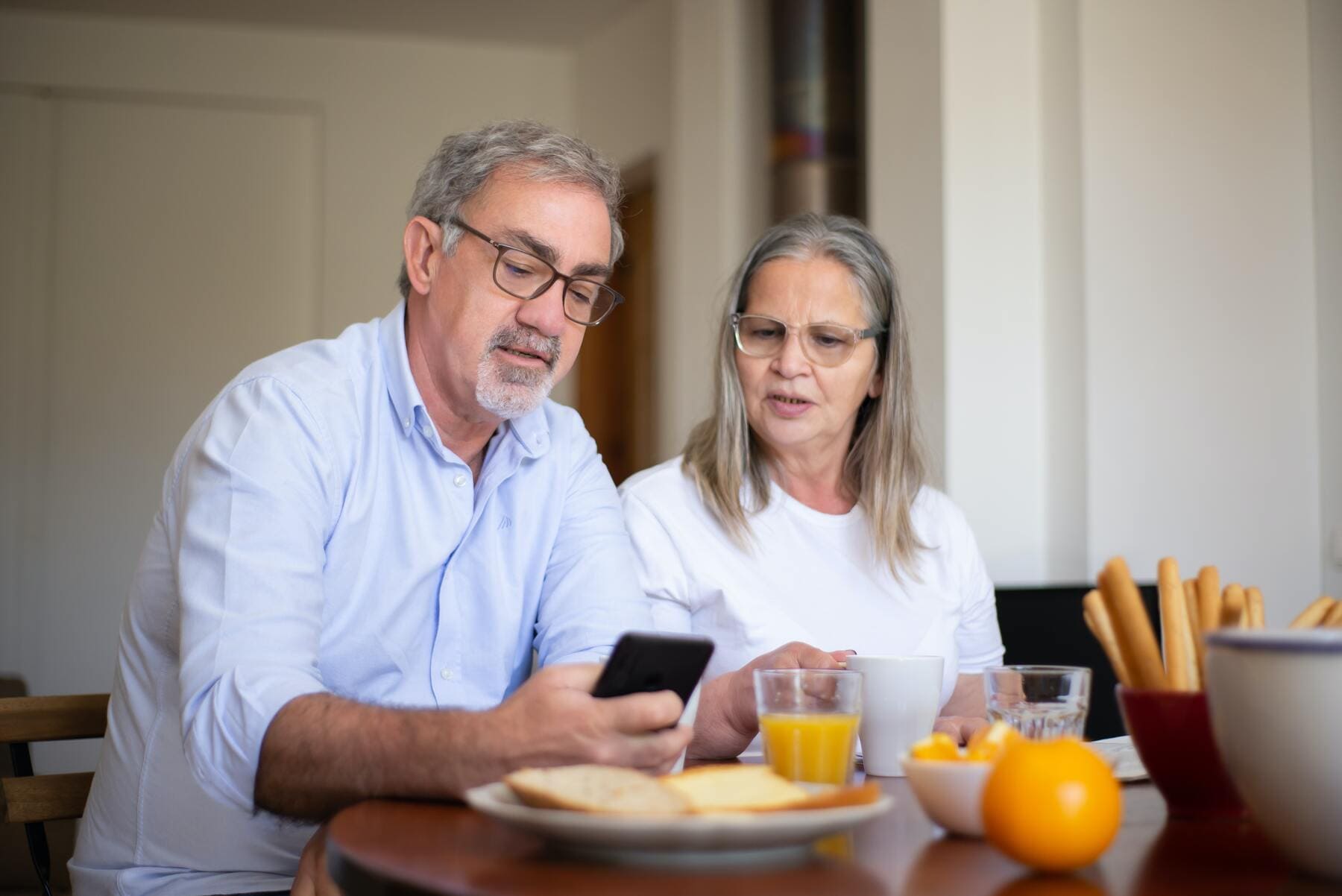 Una pareja sentada en una mesa, con el móvil en la mano y desayunando saludable