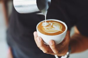 Beneficios del café: un hombre sirve una taza y realiza una flor con la leche