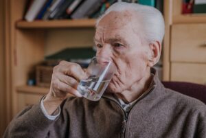 Anciano bebiendo un vaso de agua para aliviar los síntomas de hernia de hiato