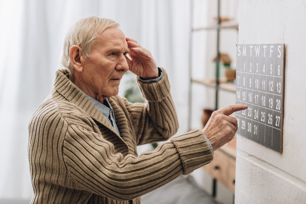Un anciano confundido ante una pizarra con letras y números. 