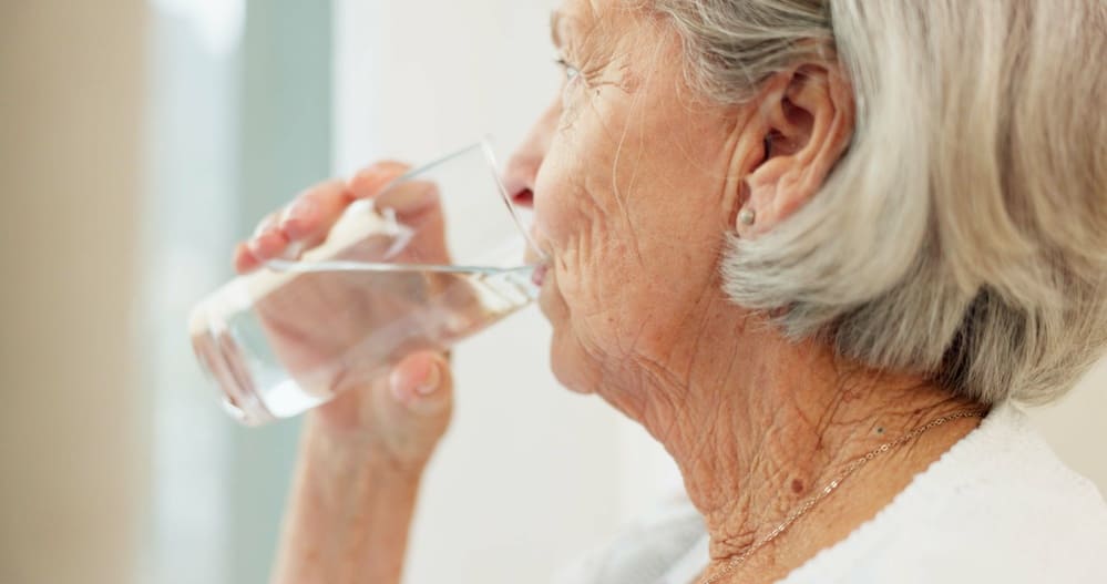 Una señora mayor bebe un vaso de agua. 