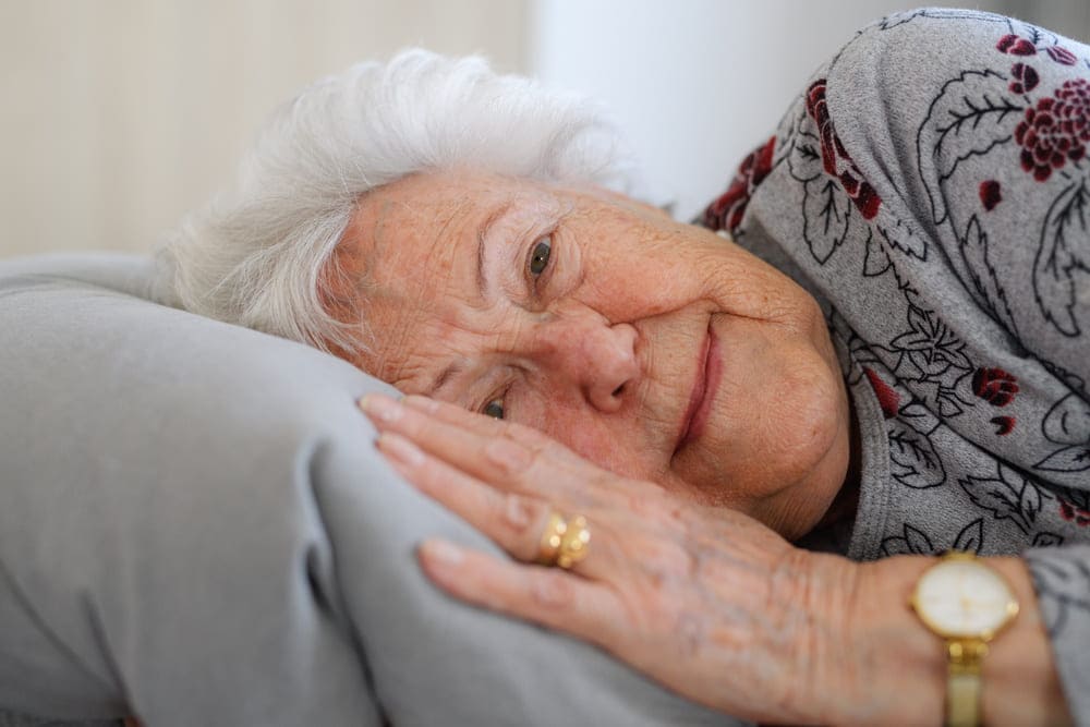 Una señora mayor está tumbada de costado en su cama con los ojos abiertos. 