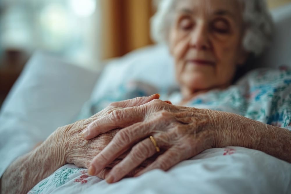 Una anciana tumbada boca arriba y durmiendo en su cama, con las manos entrelazadas.