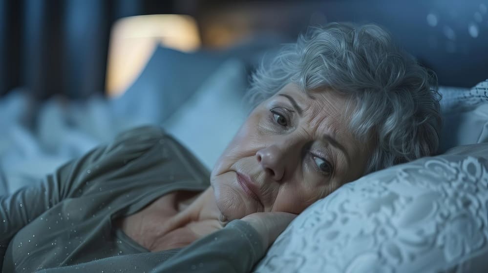 Una señora mayor postrada en su cama con la mirada perdida, triste. 