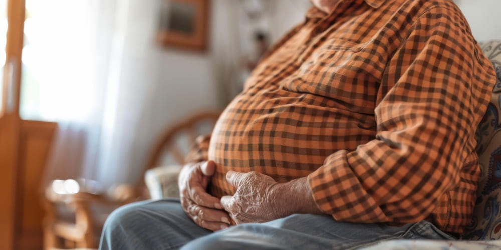 Un hombre mayor con bastante barriga sentado en el sofá de su casa. 
